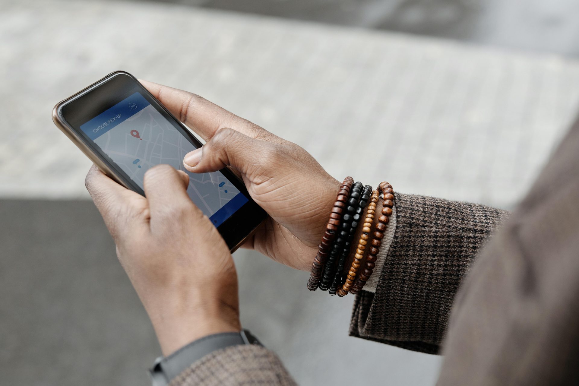 Nahaufnahme von Händen mit Armbändern, die im Freien mit einer GPS-App auf einem Smartphone navigieren.