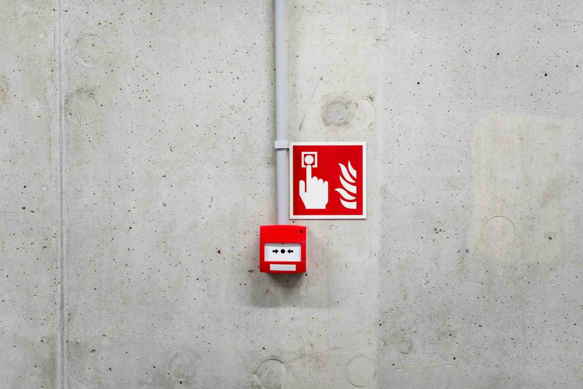 Ein roter Feueralarm an einer grauen Betonwand in Poznań erhöht das Sicherheitsbewusstsein.